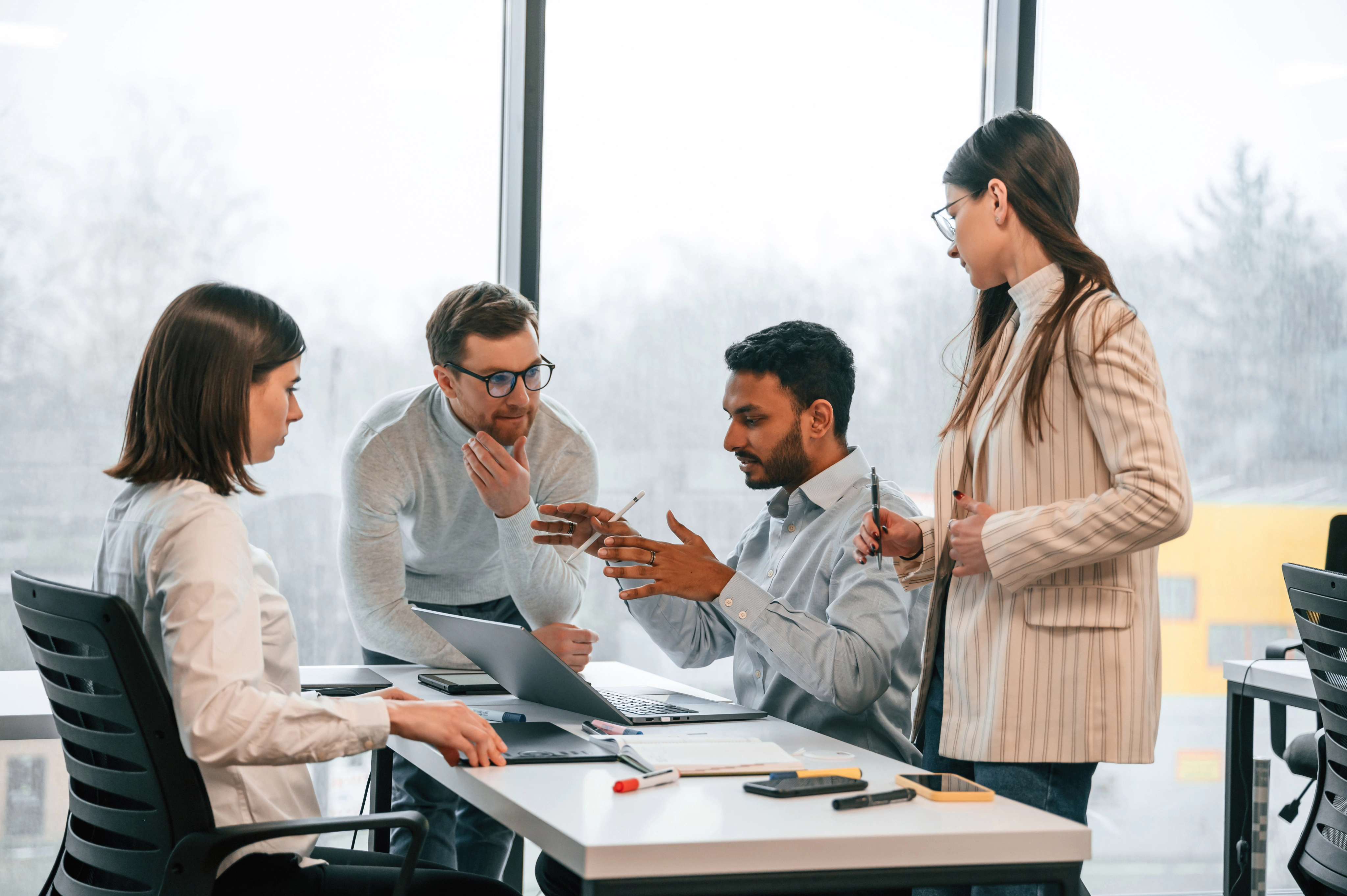 Four colleagues collaborating around a laptop in a bright office
